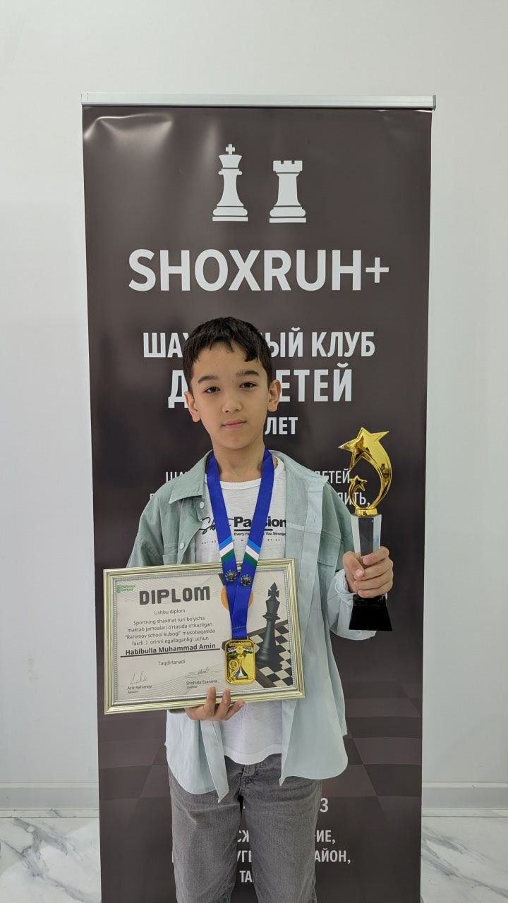 Yosh shaxmatchi kubok va diplom bilan ShoxRuh+ banneri oldida